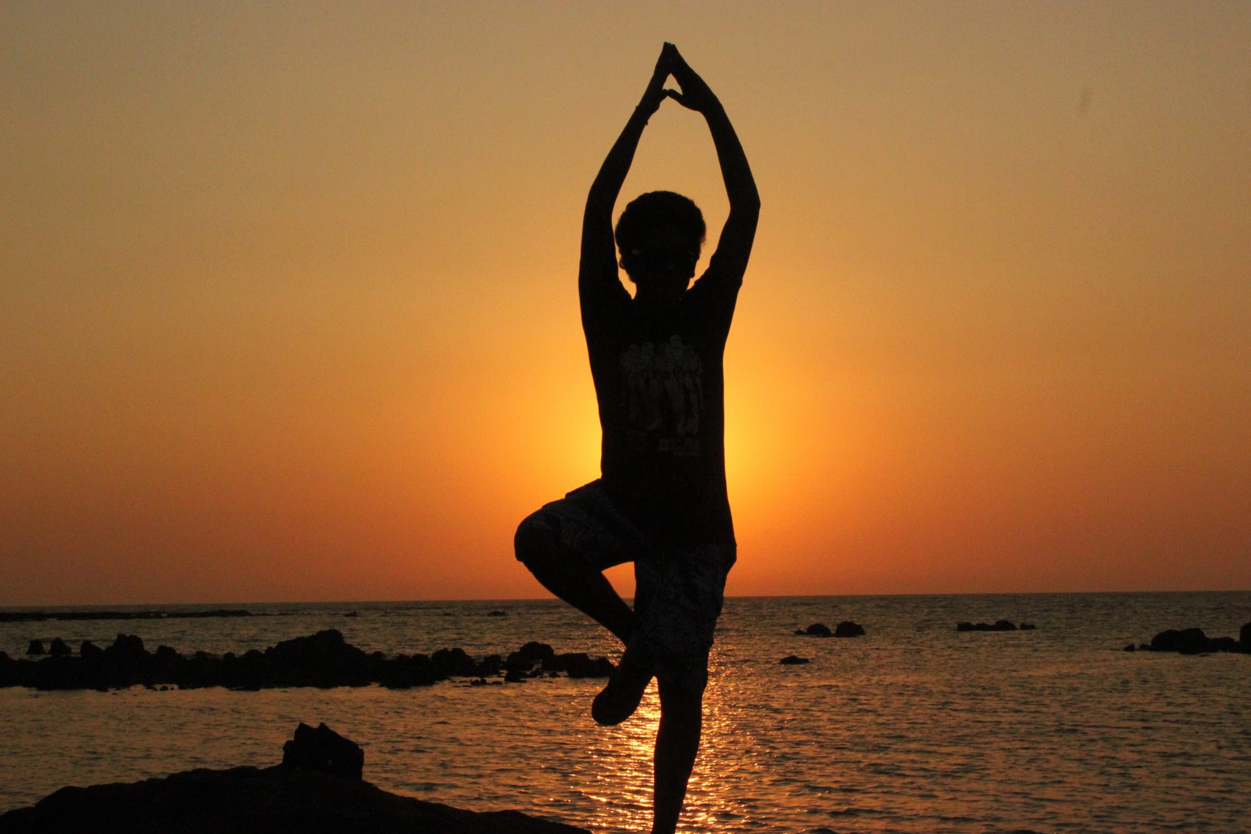 Person i yoga position ved solnedgang ved havet.