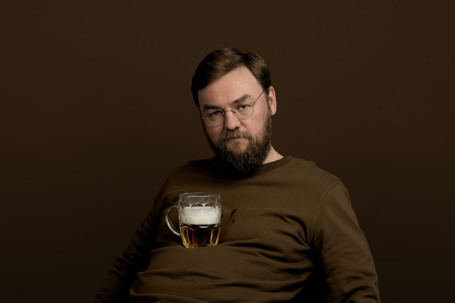 Jonas Mogensen med øl Mand med brunt tøj og ølglas på maven.
