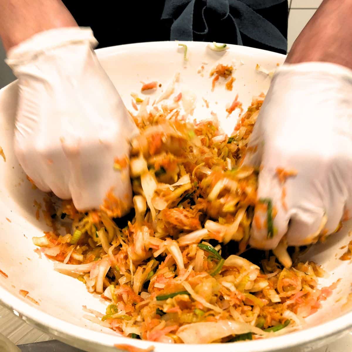 Traditionel kimchi fermentering Hånd, der laver kimchi i en stor skål til fermentering.
