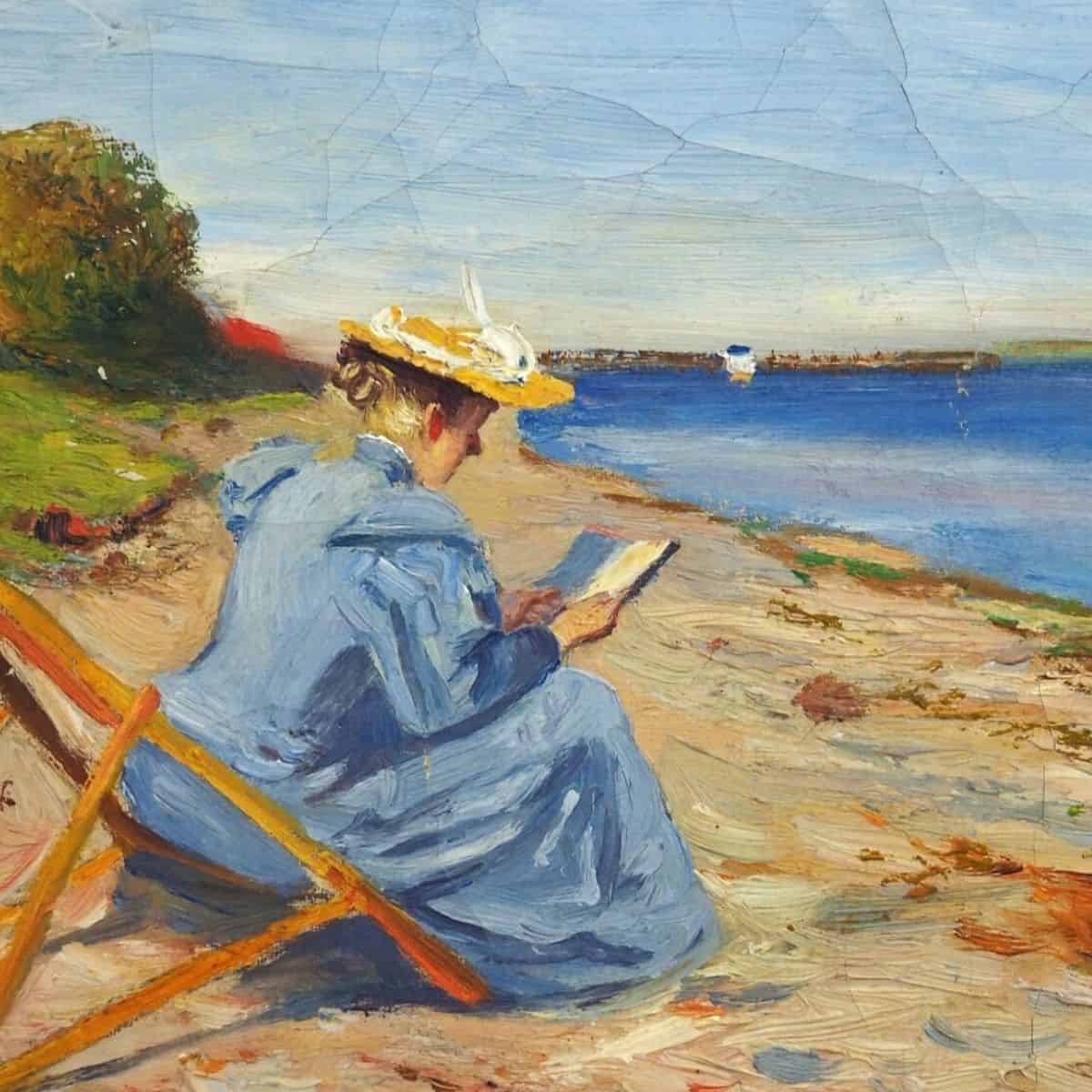 Kvindelig maler ved stranden Kvinde i blå kjole læser ved strandkanten med båd i baggrunden.