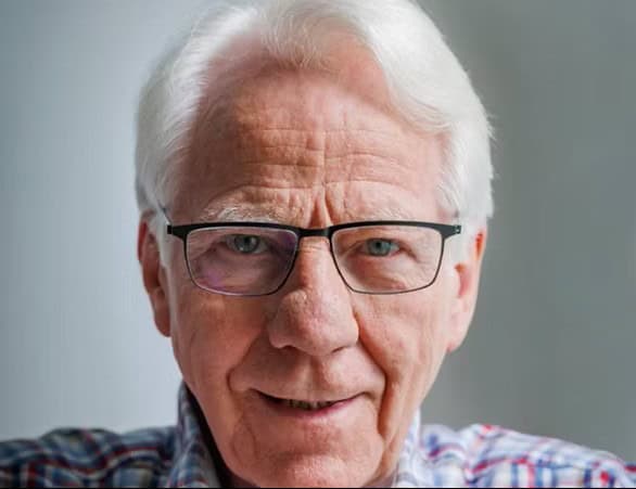 Ældre mand med briller smiler til kameraet.