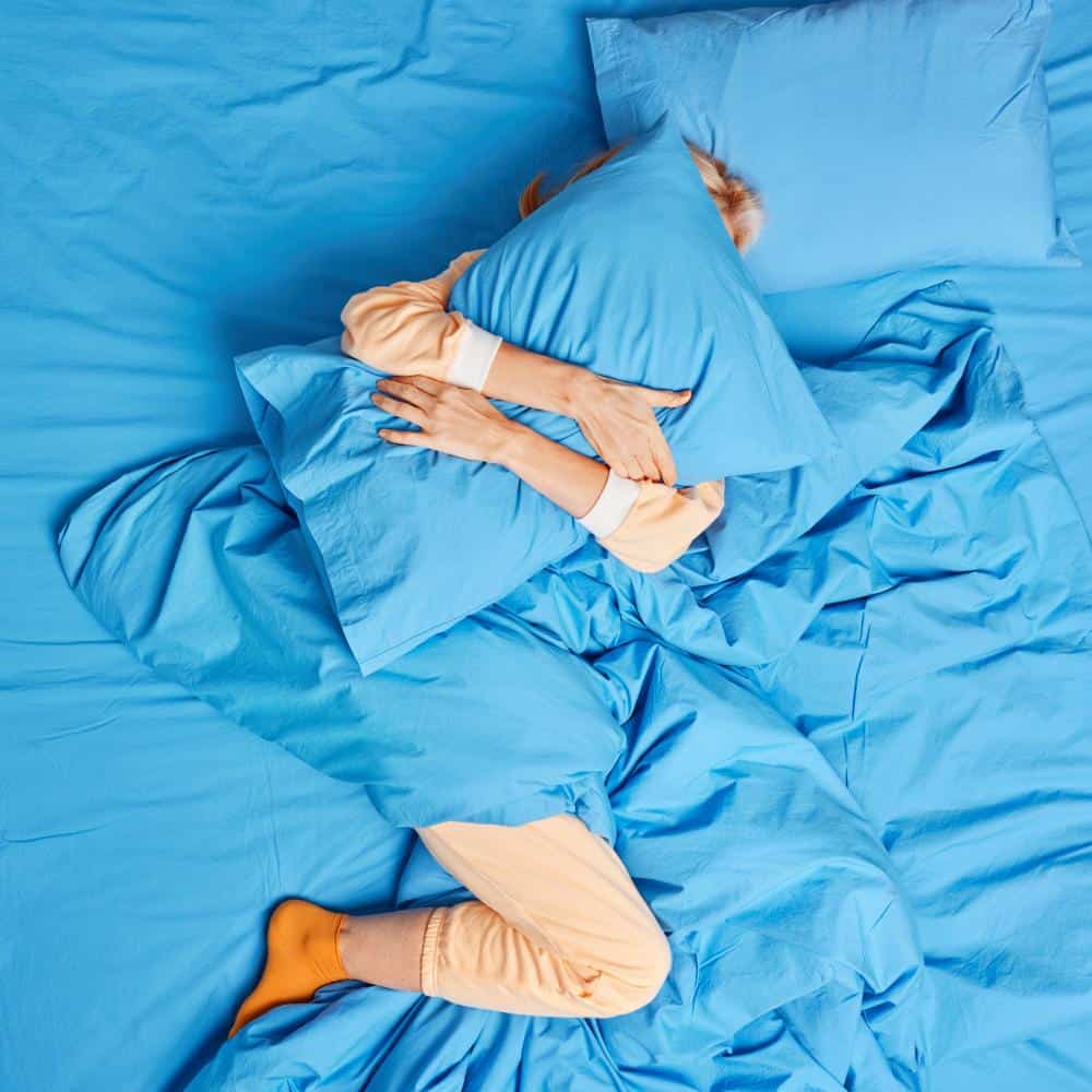 Person sover fredeligt i en blå seng med komfortable lagner.