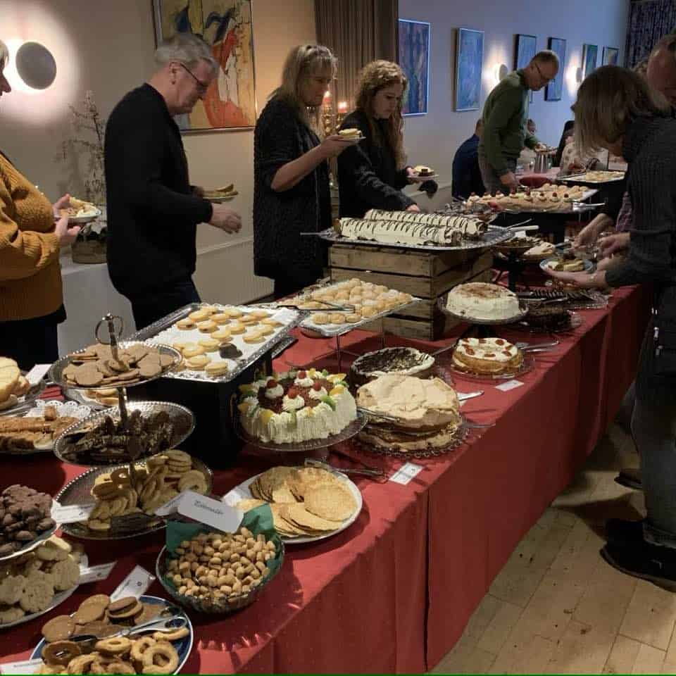 Billede af et kaffebord med forskellige kager og gæster.