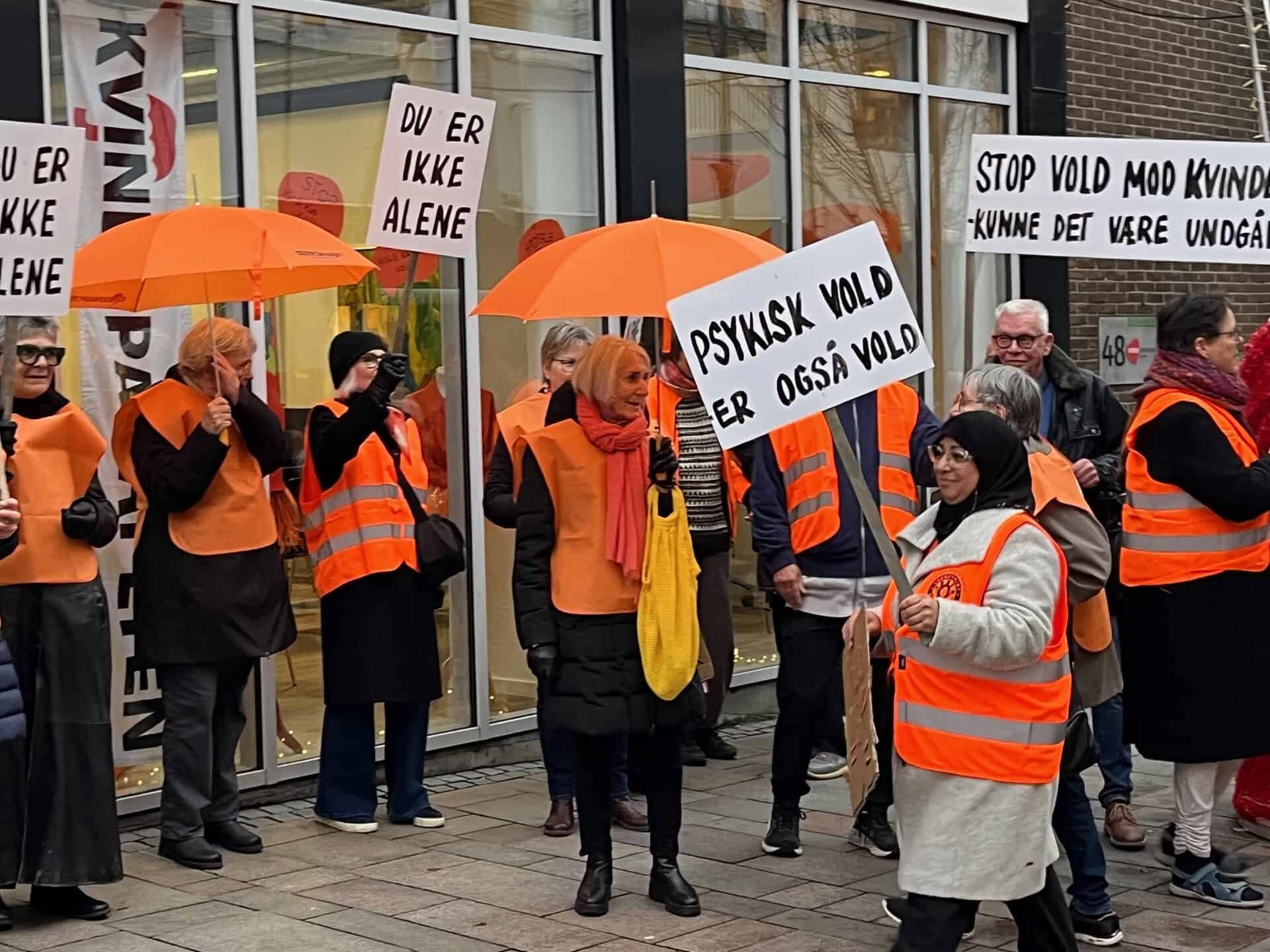 Folk protesterer mod psykisk vold med skilte og orange paraplyer.
