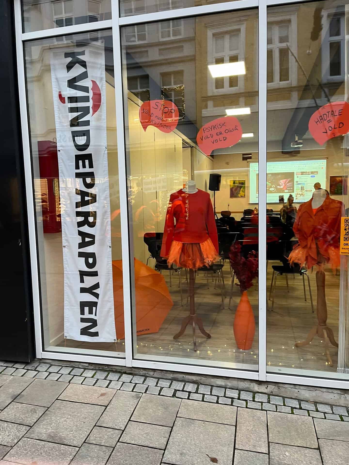 Vinduesudstilling med orange kjoler og skilte i Sonderborg.