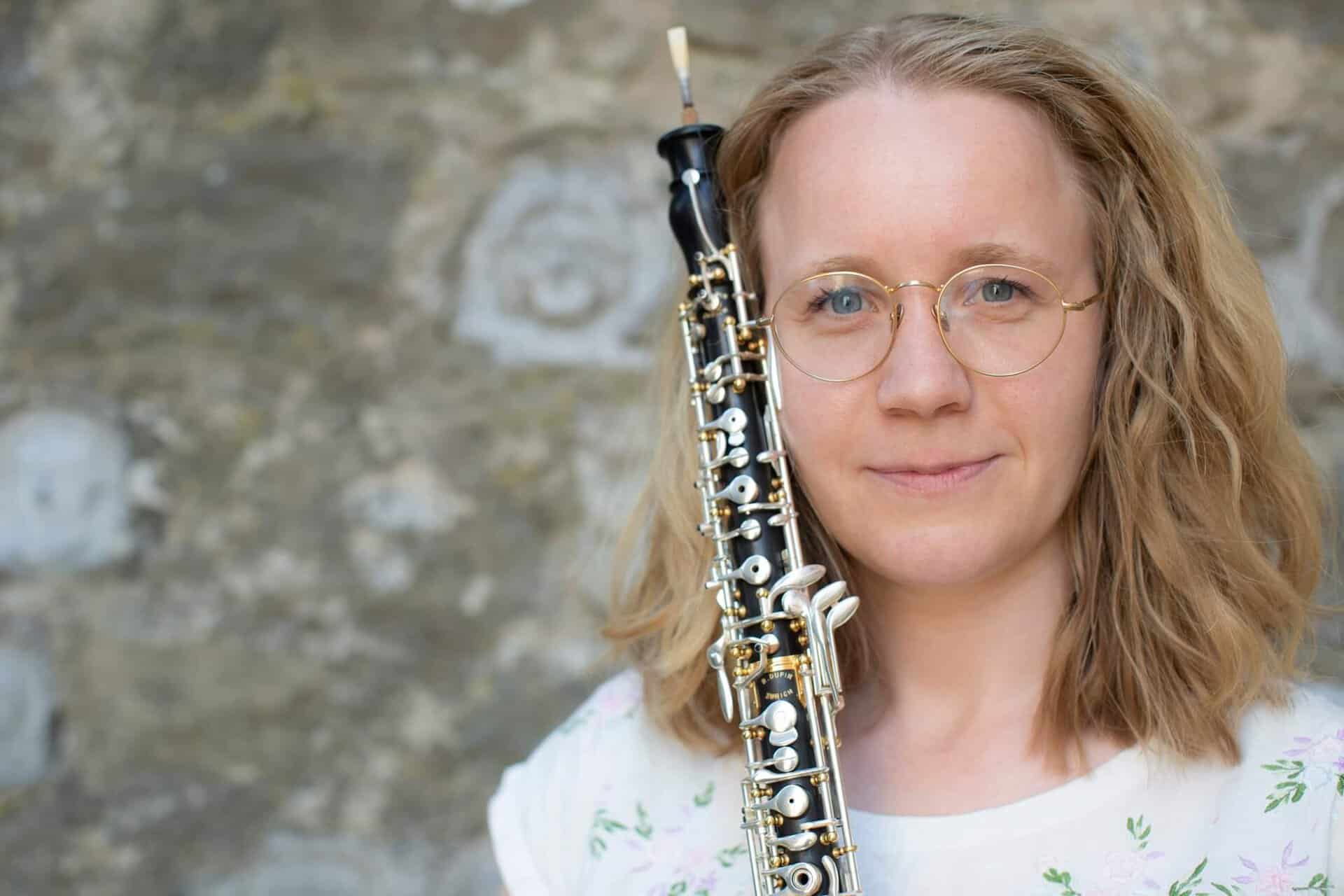 Kvinde med klarinet foran stenmur, musik og kultur i fokus.